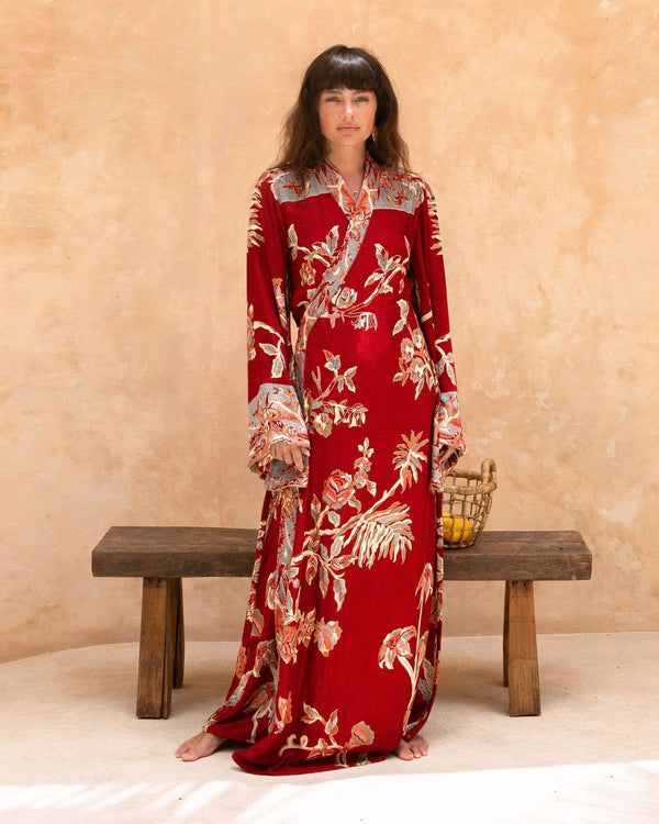 Woman in red floral robe with bell sleeves, standing barefoot near wooden bench and woven basket
