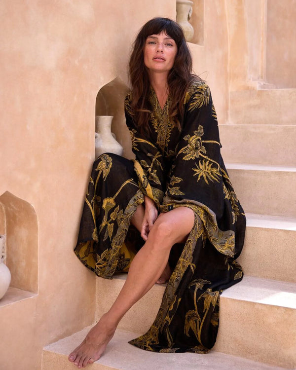 Woman in black and gold floral robe sitting on stone steps, exuding elegance and grace.