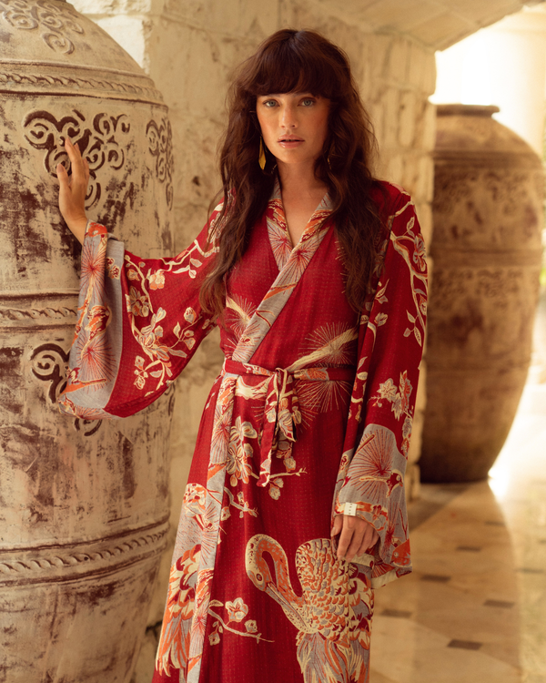 Woman in red floral kimono robe with crane print, standing beside ornate ceramic vase