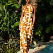 Woman in orange and white abstract print halter maxi dress by poolside tropical garden