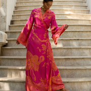 Woman in vibrant pink floral wrap dress with crane print, standing on stone stairs, exuding grace and confidence.
