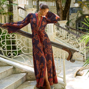 Woman in elegant floral wrap dress with long sleeves, standing on ornate stone stairs amidst lush greenery