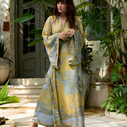 Woman in elegant yellow and blue crane-print robe by poolside, surrounded by lush tropical greenery