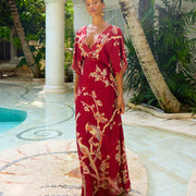 Woman in red floral maxi dress with birds, standing by poolside under palm trees